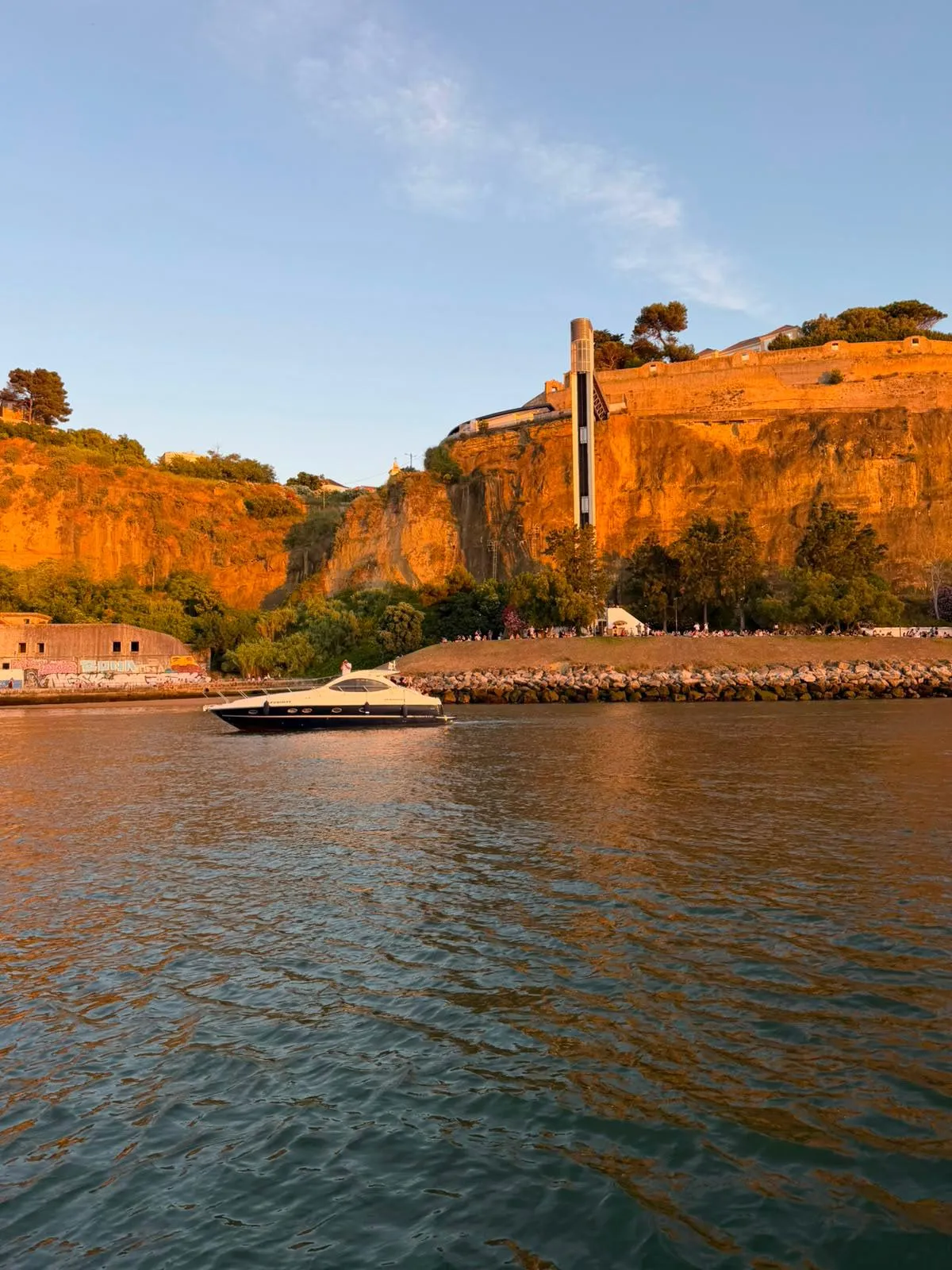 Luxury yacht cruising the Tagus at sunset beneath golden cliffs